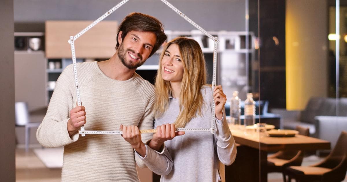 Een jong stel houdt een duimstok in de vorm van een huis omhoog