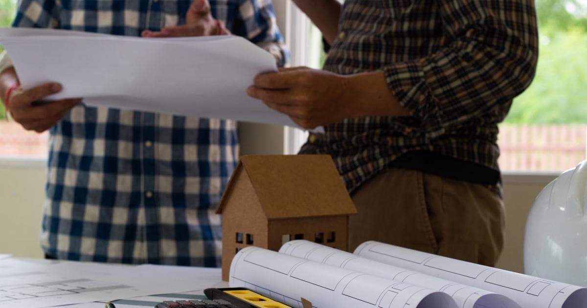 Twee mensen bekijken bouwtekeningen naast een maquette van een huis